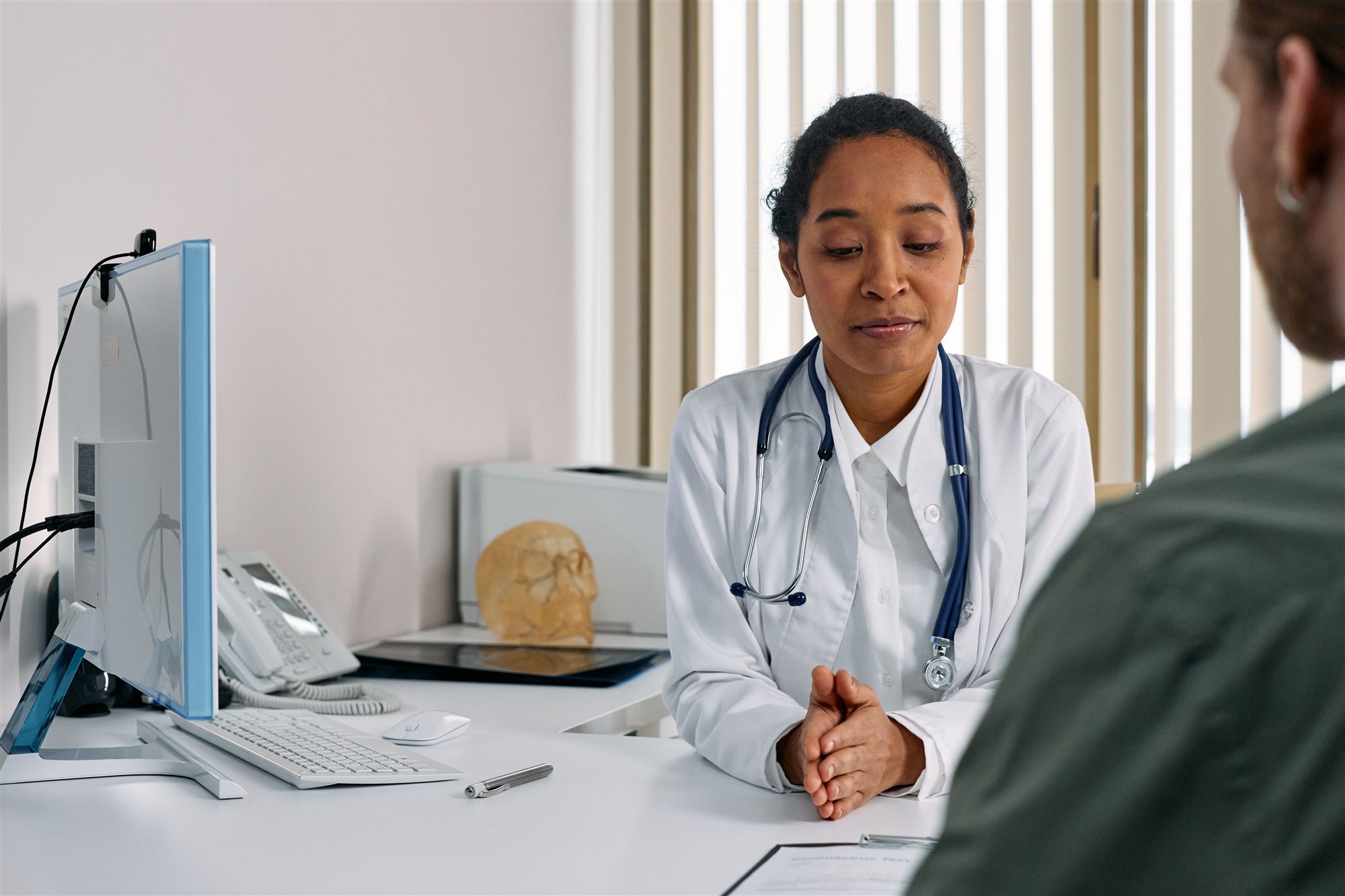 A clinician in a white coat consulting with a patient across a desk